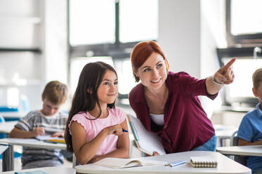 Ein freundlicher Lehrer, der im Unterricht zwischen kleinen Schulkindern umhergeht, erklärt und hilft. - HPIF24994