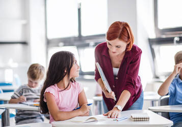 Ein freundlicher Lehrer, der im Unterricht zwischen kleinen Schulkindern umhergeht, erklärt und hilft. - HPIF24995