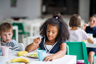 Eine Gruppe fröhlicher kleiner Schulkinder in der Kantine, die zu Mittag essen und sich unterhalten. - HPIF25007