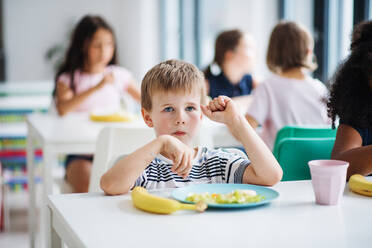 Eine Gruppe fröhlicher kleiner Schulkinder in der Kantine, die zu Mittag essen und sich unterhalten. - HPIF25008