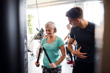 A cheerful female senior with a young trainer doing strength workout exercise in gym. - HPIF25013