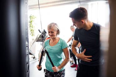Eine fröhliche weibliche Seniorin mit einem jungen Trainer macht Krafttraining Übung im Fitnessstudio. - HPIF25013