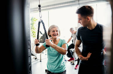 A cheerful female senior with a young trainer doing strength workout exercise in gym. - HPIF25014