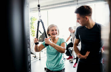 Eine fröhliche weibliche Seniorin mit einem jungen Trainer macht Krafttraining Übung im Fitnessstudio. - HPIF25014