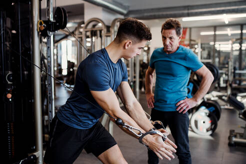 Ein älterer Mann mit einem jungen männlichen Trainer macht Krafttraining Übung im Fitnessstudio. - HPIF25017