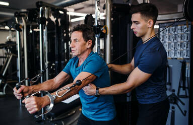 Ein älterer Mann mit einem jungen männlichen Trainer macht Krafttraining Übung im Fitnessstudio. - HPIF25023