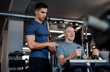 Ein älterer Mann mit einem jungen männlichen Trainer macht Krafttraining Übung im Fitnessstudio. - HPIF25034