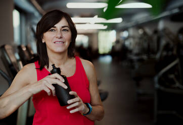 Eine zufriedene ältere Frau mit einer Wasserflasche im Fitnessstudio, die sich nach dem Training ausruht. Kopierraum. - HPIF25046