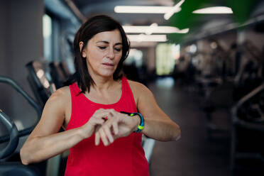 Eine zufriedene ältere Frau mit einer Smartwatch im Fitnessstudio, die sich nach dem Training ausruht und die Zeit überprüft. Copy space. - HPIF25047