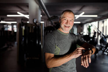 Ein fröhlicher älterer Mann mit Smartwatch im Fitnessstudio, der die Zeit misst, während er trainiert. - HPIF25062