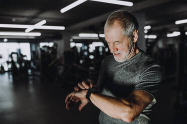 Ein fröhlicher älterer Mann mit Smartwatch im Fitnessstudio, der die Zeit misst, während er trainiert. - HPIF25064