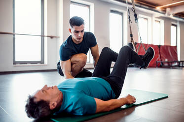 A senior man in gym and a handsome personal trainer doing exercise with TRX. - HPIF25078