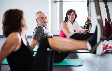 Eine Gruppe fröhlicher Senioren im Fitnessstudio, die mit TRX trainieren und sich unterhalten. - HPIF25082