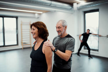 A cheerful senior woman in gym doing exercise with a personal trainer. - HPIF25094