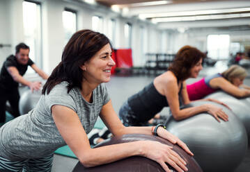 Eine Gruppe fröhlicher Seniorinnen in einem Fitnessstudio, die Übungen auf Fitbällen machen. - HPIF25098