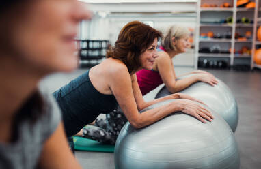 Eine Gruppe fröhlicher Seniorinnen in einem Fitnessstudio, die Übungen auf Fitbällen machen. - HPIF25102
