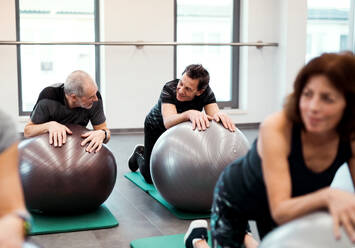 Eine Gruppe fröhlicher Seniorinnen in einem Fitnessstudio, die Übungen auf Fitbällen machen. - HPIF25103