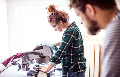 Kleiner Betrieb eines jungen Paares: Mann und Frau arbeiten mit einer Schleifmaschine in der Tischlerwerkstatt. - HPIF25151