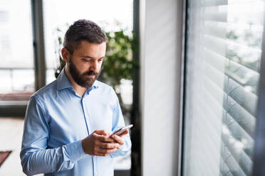 Ein gut aussehender Mann mit einem Smartphone am Fenster, der eine SMS schreibt. - HPIF25234