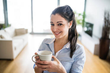 A happy woman holding a cup of coffee at home. - HPIF25241