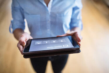 Eine unerkennbare Frau hält ein Tablet mit einem intelligenten Haussteuerungssystem. - HPIF25244