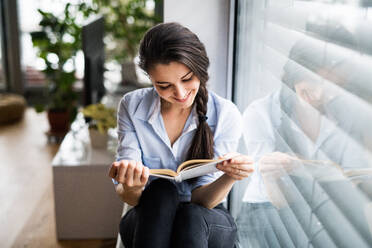 Eine Frau sitzt am Fenster und liest ein Buch. - HPIF25254