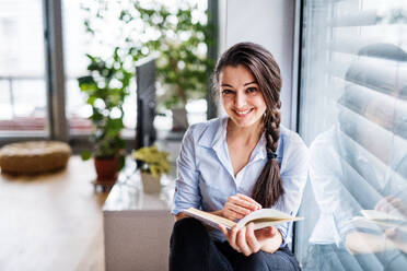 A woman sitting by the window, reading a book. Smart home control system. - HPIF25255