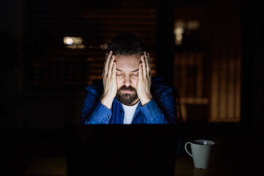 Ein müder Mann, der nachts zu Hause an einem Laptop arbeitet. - HPIF25263
