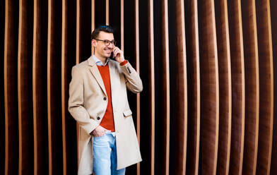 Junger, gut aussehender Mann mit Smartphone, der an einer Holzwand steht und einen Anruf tätigt. - HPIF25281