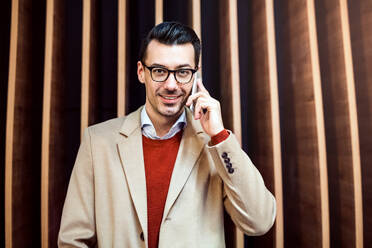 Young handsome man with smartphone standing against wooden wall, making a phone call. - HPIF25282