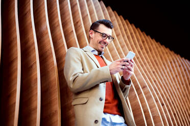 Young handsome man with smartphone standing against wooden wall, texting. - HPIF25283