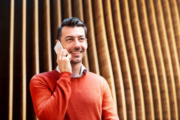 Young handsome man with smartphone standing against wooden wall, making a phone call. - HPIF25284