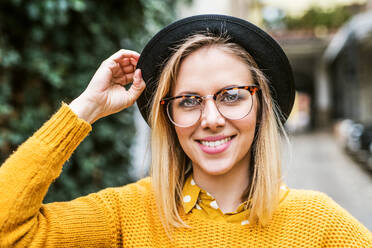 Porträt einer jungen Frau mit schwarzem Hut und Brille in einer sonnigen Frühlingsstadt. - HPIF25289