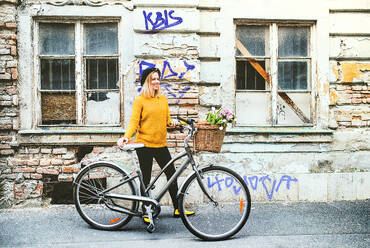 Portrait of a young beautiful woman with bicycle standing against old building. Sunny spring town. - HPIF25291