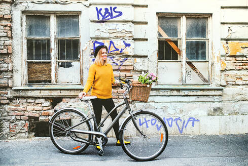 Porträt einer jungen schönen Frau mit Fahrrad vor einem alten Gebäude in einer sonnigen Frühlingsstadt. - HPIF25291