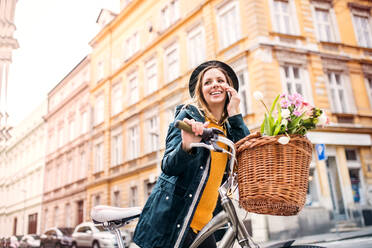 Junge schöne Frau mit Fahrrad und Smartphone in der Stadt, die telefoniert. Sonniger Frühling. - HPIF25296