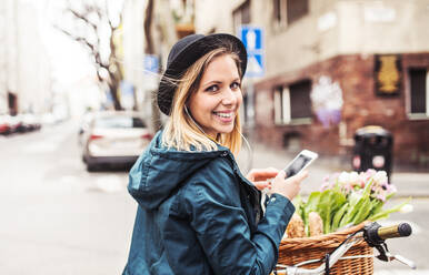 Junge schöne Frau mit Fahrrad und Smartphone in der Stadt, SMS schreiben. Sonniger Frühling. - HPIF25297