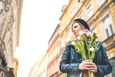 Porträt einer jungen schönen Frau mit Blumen in der Stadt, sonniger Frühling, Raum kopieren. - HPIF25304