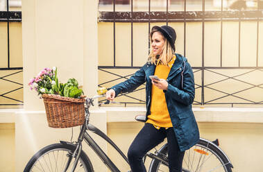 Junge schöne Frau mit Fahrrad und Smartphone in der Stadt, SMS schreiben. Sonniger Frühling. - HPIF25308