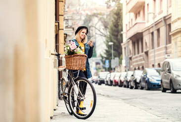 Junge schöne Frau mit Fahrrad und Smartphone in der Stadt, SMS schreiben. Sonniger Frühling. - HPIF25309