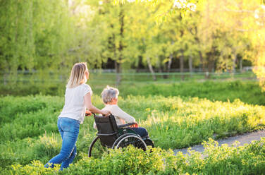 Ältere Großmutter im Rollstuhl mit einer erwachsenen Enkelin draußen in der Natur im Frühling. - HPIF25347