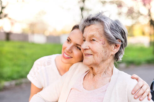 Ältere Großmutter und eine erwachsene Enkelin draußen in der Natur, die sich umarmen. - HPIF25351