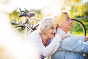 Schönes älteres Paar mit Fahrrädern draußen in der frühlingshaften Natur unter blühenden Bäumen. - HPIF25371