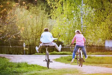 Beautiful senior couple with bicycles cycling outside in spring nature, having fun. Rear view. - HPIF25390