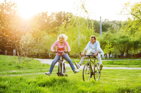 Beautiful senior couple with bicycles cycling outside in spring nature, having fun. - HPIF25392