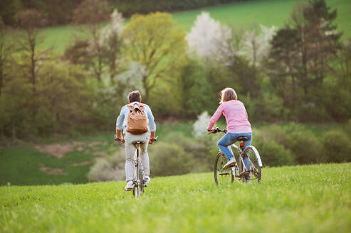 Beautiful senior couple outside in spring nature, with bicycles cycling on grassland. Rear view. - HPIF25401