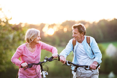 Beautiful senior couple with bicycles outside in spring nature cycling. - HPIF25405
