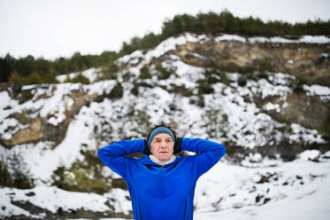 Ein Porträt eines älteren Mannes, der sich vor dem Lauf in der winterlichen Natur dehnt, in Hüfthöhe, Kopierraum. - HPIF25414