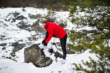 Eine ältere Läuferin beim Binden der Schnürsenkel in der winterlichen Natur, Fuß auf Fels. - HPIF25422