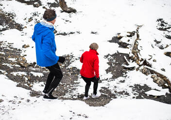 Blick auf ein älteres Paar in voller Länge, das in verschneiter Winterlandschaft bergab läuft. - HPIF25425